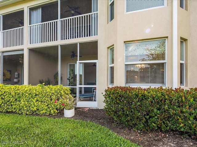 property entrance with a balcony, a ceiling fan, and stucco siding