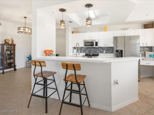 kitchen featuring a kitchen breakfast bar, a sink, a tray ceiling, stainless steel appliances, and backsplash