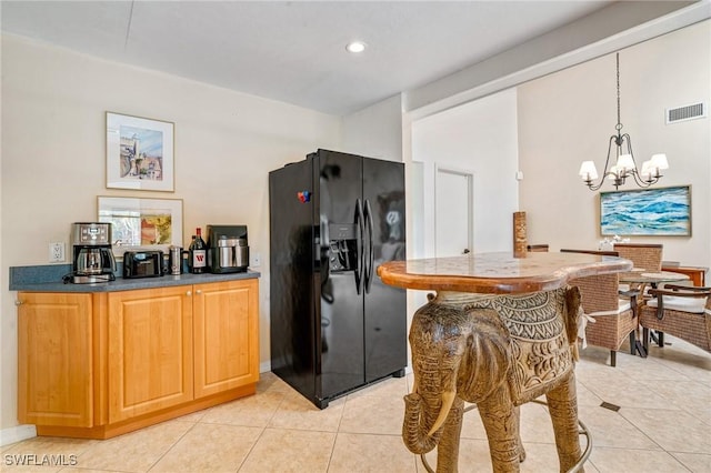 kitchen featuring light tile patterned floors, a chandelier, visible vents, hanging light fixtures, and black fridge