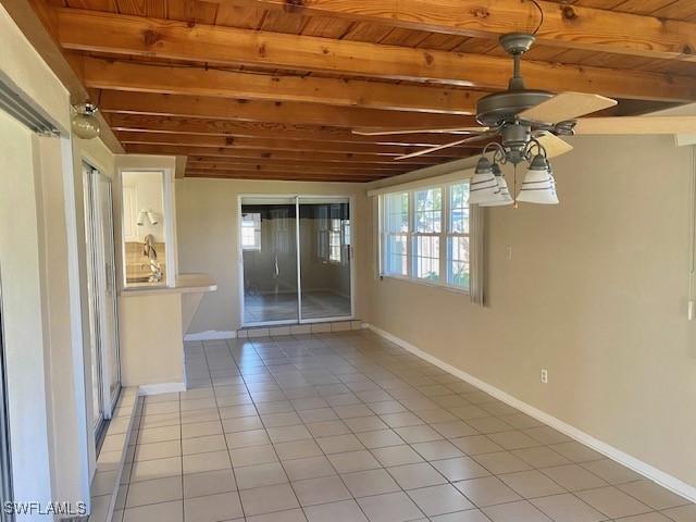 empty room featuring ceiling fan, light tile patterned floors, wooden ceiling, baseboards, and beamed ceiling