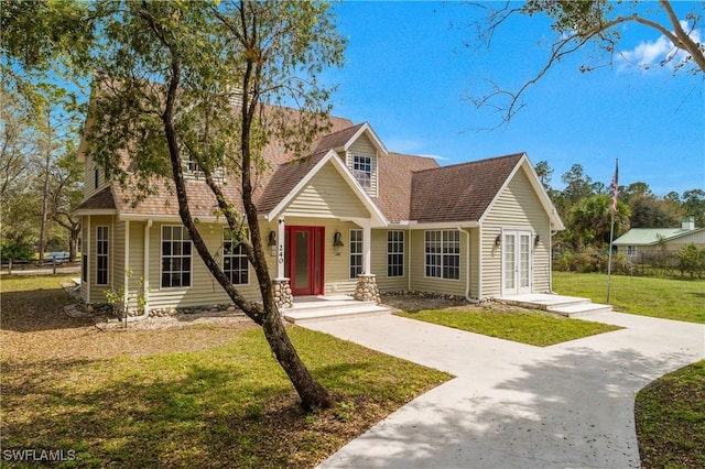 cape cod home featuring a shingled roof, concrete driveway, and a front lawn