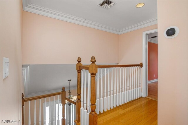 hall with wood finished floors, ornamental molding, an upstairs landing, and visible vents