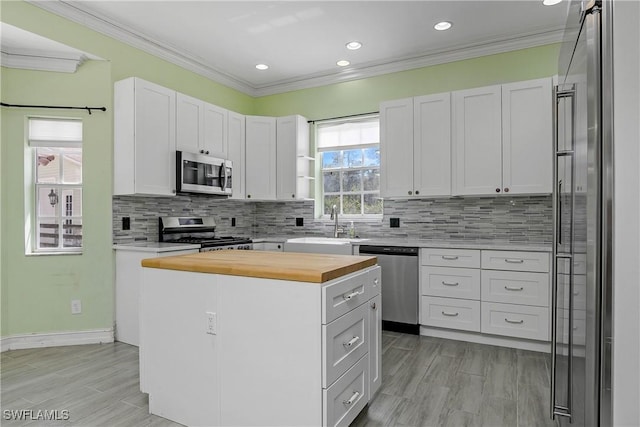 kitchen featuring butcher block countertops, a sink, ornamental molding, appliances with stainless steel finishes, and a center island