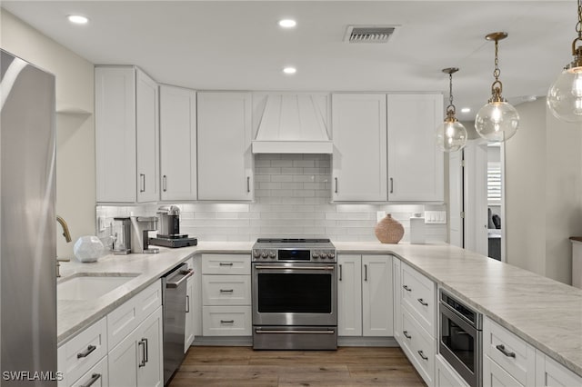 kitchen with premium range hood, appliances with stainless steel finishes, visible vents, and white cabinetry