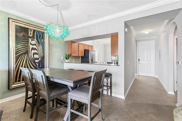 tiled dining space with arched walkways, ornamental molding, a chandelier, and baseboards