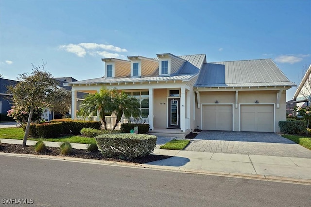 view of front of house with decorative driveway, stucco siding, a porch, a standing seam roof, and a garage