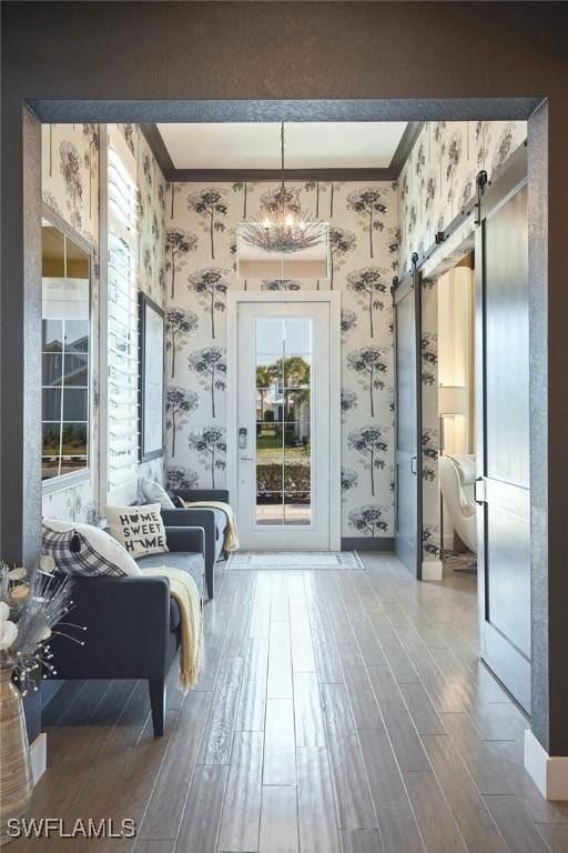 entryway featuring ornamental molding, wood finished floors, a barn door, and wallpapered walls