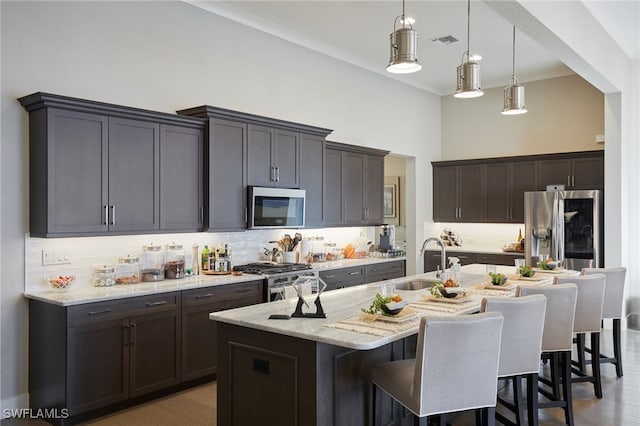 kitchen featuring a breakfast bar area, visible vents, appliances with stainless steel finishes, a kitchen island with sink, and a sink