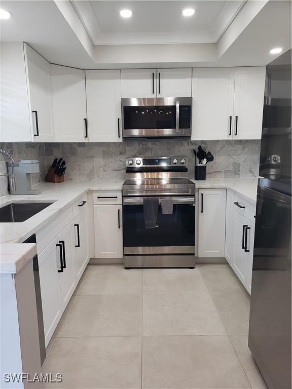 kitchen featuring light tile patterned floors, a sink, stainless steel appliances, white cabinets, and tasteful backsplash