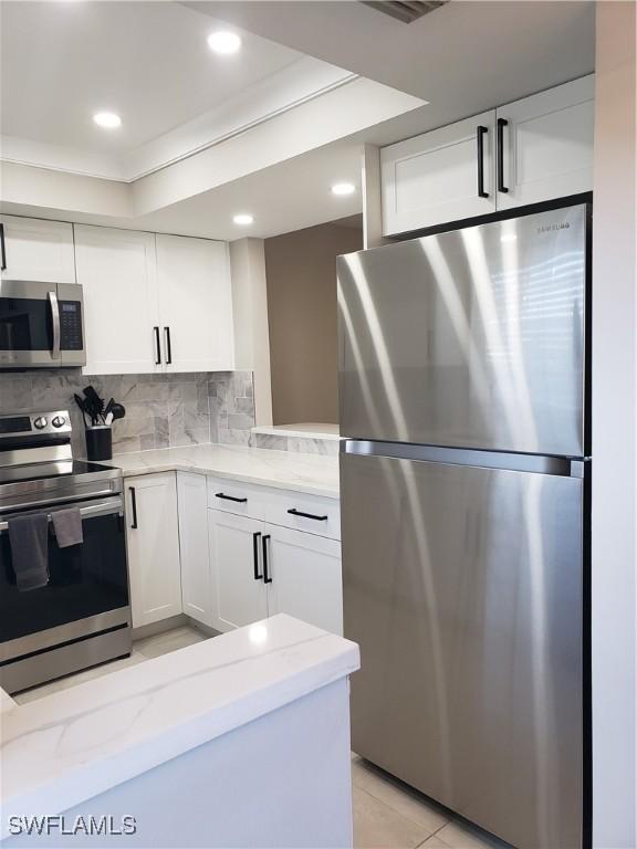 kitchen featuring stainless steel appliances, tasteful backsplash, light stone countertops, and white cabinets