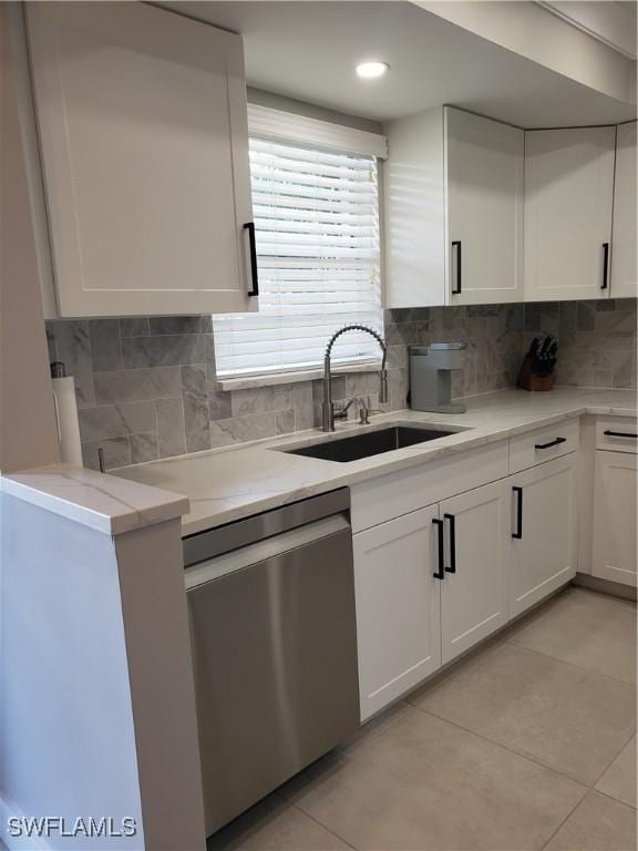 kitchen with light tile patterned floors, white cabinets, decorative backsplash, stainless steel dishwasher, and a sink