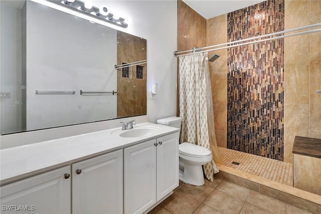 bathroom featuring toilet, tile patterned floors, a tile shower, and vanity