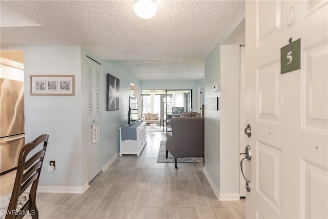 hall with a textured ceiling, light wood-style flooring, and baseboards