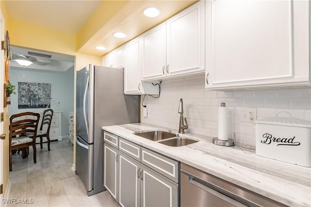 kitchen with a sink, white cabinetry, freestanding refrigerator, light stone countertops, and tasteful backsplash