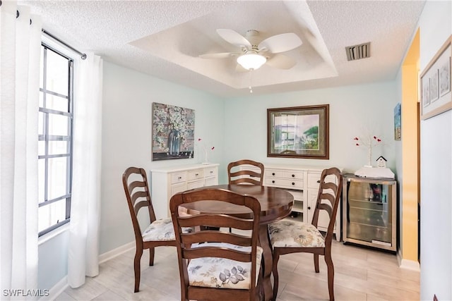 dining area featuring a healthy amount of sunlight, beverage cooler, visible vents, and a raised ceiling