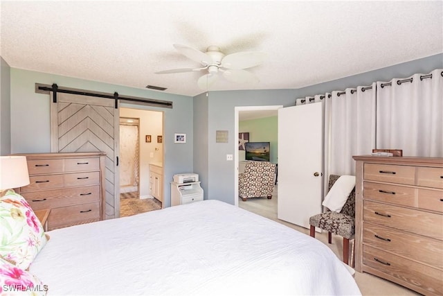 bedroom with visible vents, a textured ceiling, ensuite bathroom, and a barn door