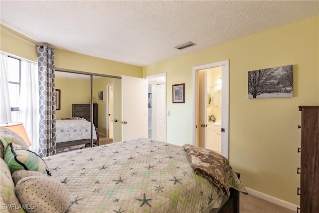 carpeted bedroom with baseboards, visible vents, ensuite bathroom, a textured ceiling, and a closet