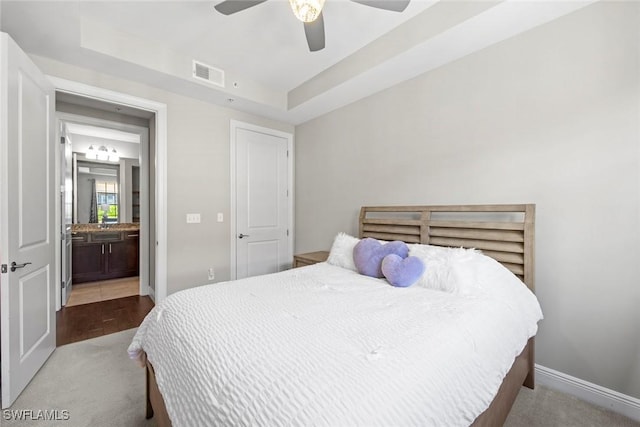 carpeted bedroom featuring baseboards, visible vents, a raised ceiling, and a ceiling fan