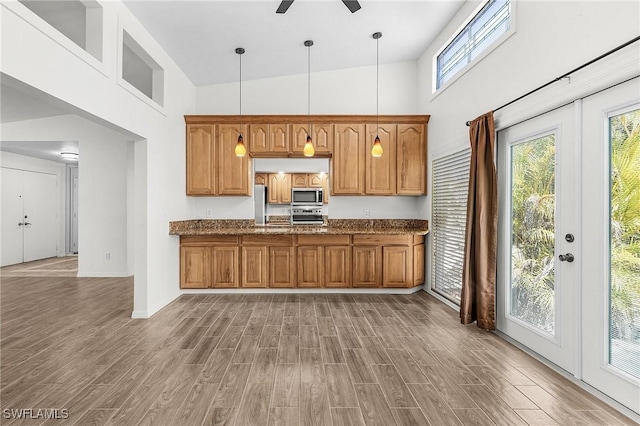 kitchen featuring appliances with stainless steel finishes, brown cabinetry, a high ceiling, and wood finished floors