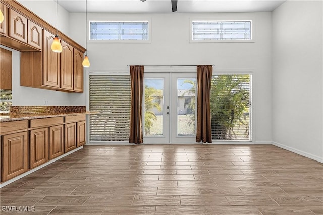 interior space with wood finished floors, a towering ceiling, baseboards, a ceiling fan, and french doors