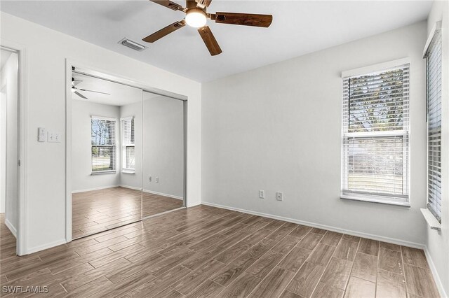 unfurnished bedroom featuring a ceiling fan, a closet, visible vents, and wood finished floors