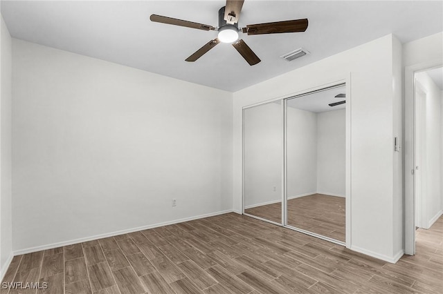 unfurnished bedroom featuring baseboards, visible vents, ceiling fan, wood finished floors, and a closet