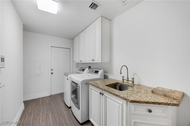 laundry room featuring dark wood finished floors, washing machine and clothes dryer, cabinet space, visible vents, and a sink