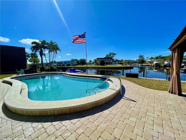 pool with a patio area, a water view, and fence