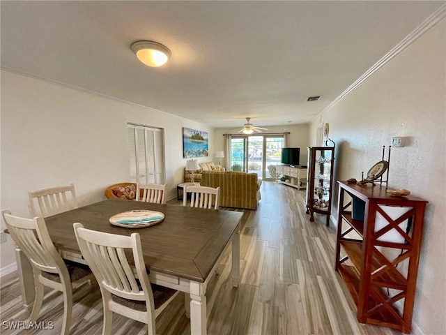 dining space with visible vents, ornamental molding, a ceiling fan, wood finished floors, and baseboards