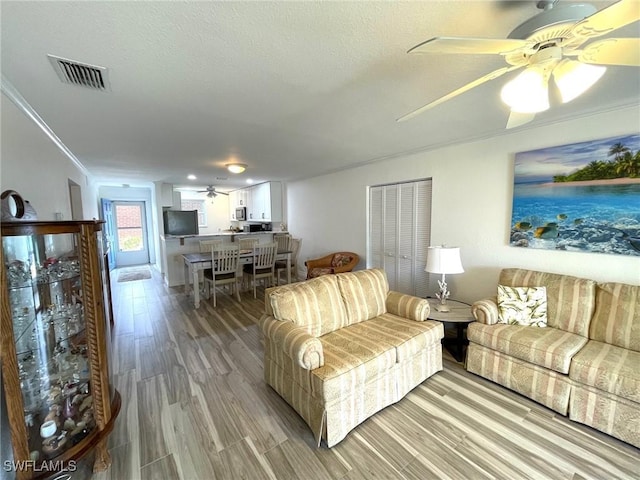 living area featuring crown molding, light wood finished floors, visible vents, ceiling fan, and a textured ceiling