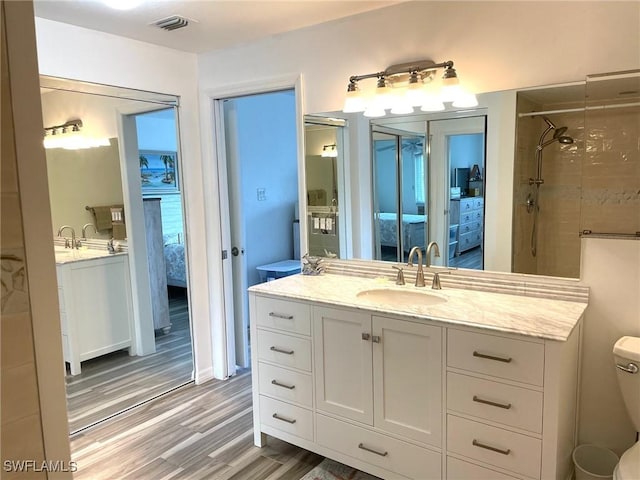 ensuite bathroom with connected bathroom, toilet, wood finished floors, vanity, and visible vents