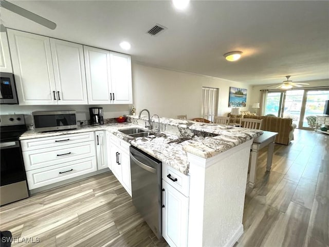 kitchen featuring open floor plan, a peninsula, stainless steel appliances, white cabinetry, and a sink