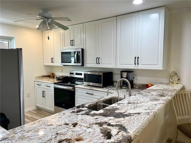 kitchen featuring a sink, a ceiling fan, white cabinetry, appliances with stainless steel finishes, and light stone countertops