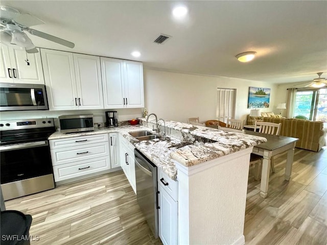 kitchen featuring a peninsula, a sink, white cabinets, open floor plan, and appliances with stainless steel finishes