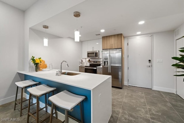 kitchen with appliances with stainless steel finishes, a peninsula, a kitchen bar, a sink, and recessed lighting