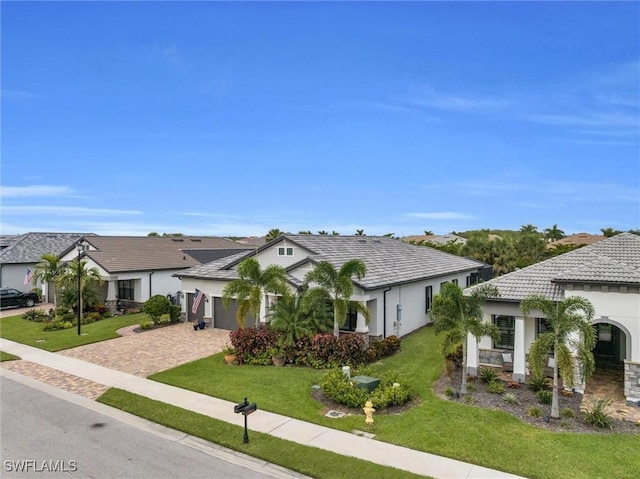 view of front facade featuring decorative driveway, stucco siding, an attached garage, a front yard, and a residential view