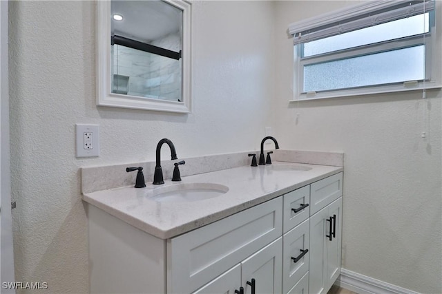 full bathroom featuring double vanity, baseboards, walk in shower, and a sink