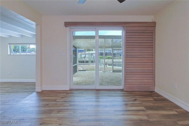 empty room featuring beam ceiling, baseboards, and wood finished floors