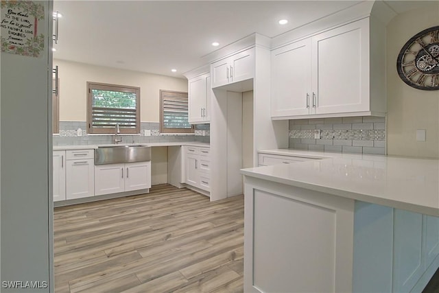 kitchen with light wood-style flooring, a sink, white cabinetry, light countertops, and decorative backsplash