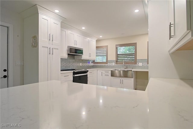 kitchen featuring range with electric stovetop, tasteful backsplash, stainless steel microwave, white cabinetry, and a sink