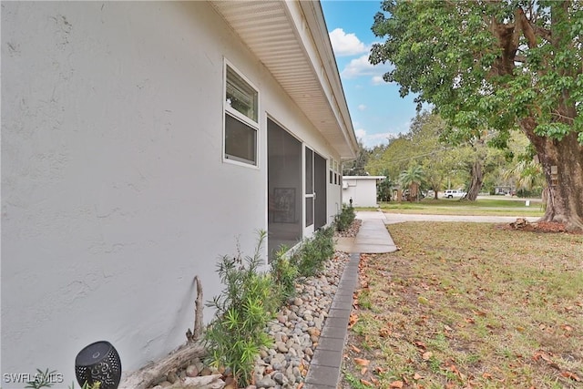 view of side of property featuring a sunroom, a yard, and stucco siding