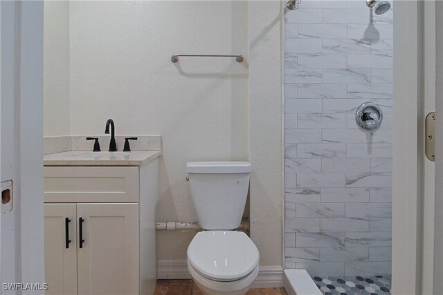 full bath featuring baseboards, a tile shower, vanity, and toilet