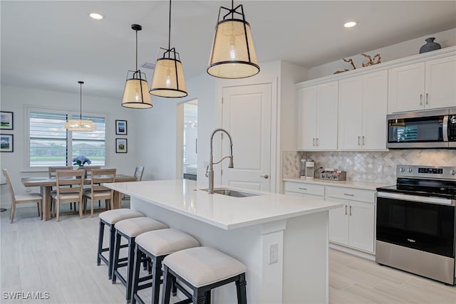 kitchen featuring a sink, a kitchen island with sink, stainless steel appliances, light countertops, and backsplash