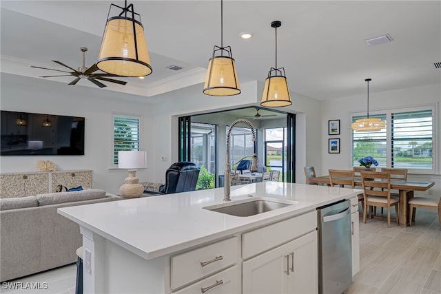 kitchen with light countertops, ornamental molding, open floor plan, a sink, and dishwasher