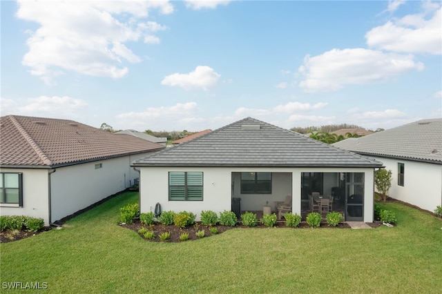 back of house featuring a lawn, a tile roof, a sunroom, and stucco siding