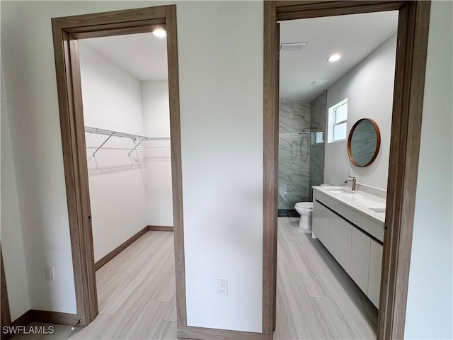 bathroom with a spacious closet, a shower stall, vanity, and baseboards