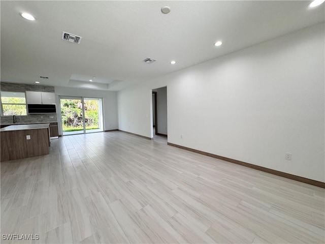 unfurnished living room featuring a tray ceiling, visible vents, light wood-style flooring, and baseboards