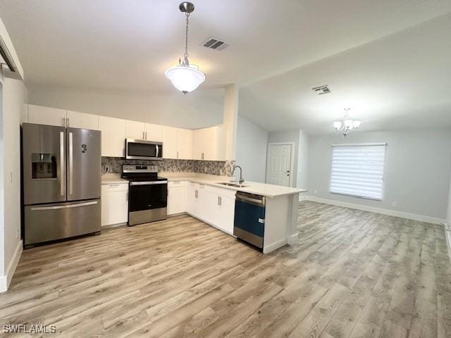 kitchen with a sink, white cabinetry, light countertops, appliances with stainless steel finishes, and decorative light fixtures