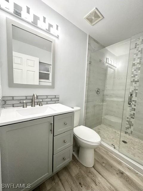 full bath featuring toilet, wood finished floors, vanity, visible vents, and a stall shower