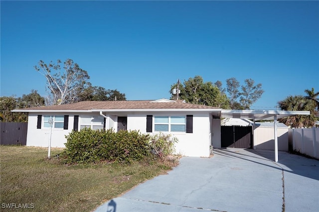 single story home with driveway, an attached carport, fence, a front lawn, and stucco siding